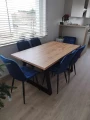 Stół Loft Trapez z drewnianym blatem i czarnymi metalowymi nogami w nowoczesnej jadalni. Aranżacja stołu z granatowymi krzesłami pokazująca jego wygląd we wnętrzu.